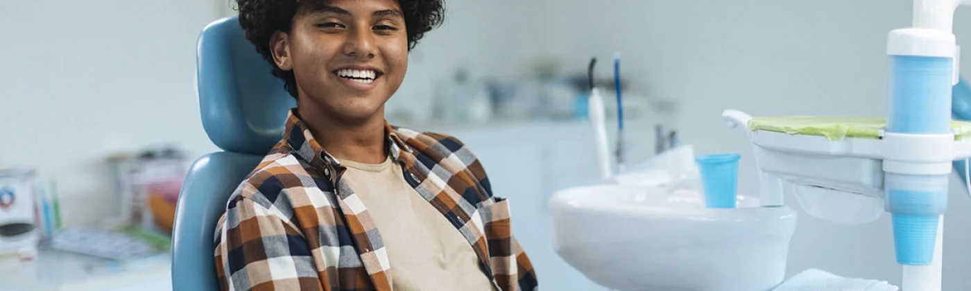 A smiling person seated in a dental chair with dental equipment in a clean clinic.